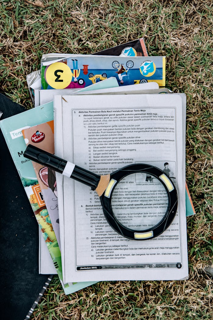 Magnifying glass on educational papers with books and grass background, outdoors.