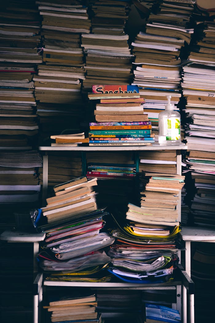Full background of messy heaps of various paperback books stacked together on white shelves in light room